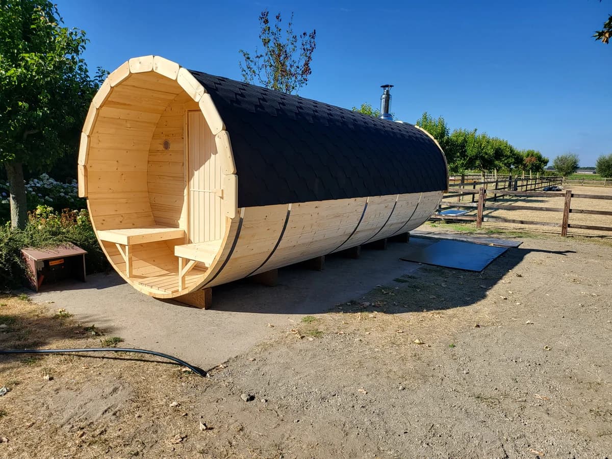 Sauna de barril ao ar livre: terraço aberto com dois bancos, telhado preto de telhas asfálticas e chaminé