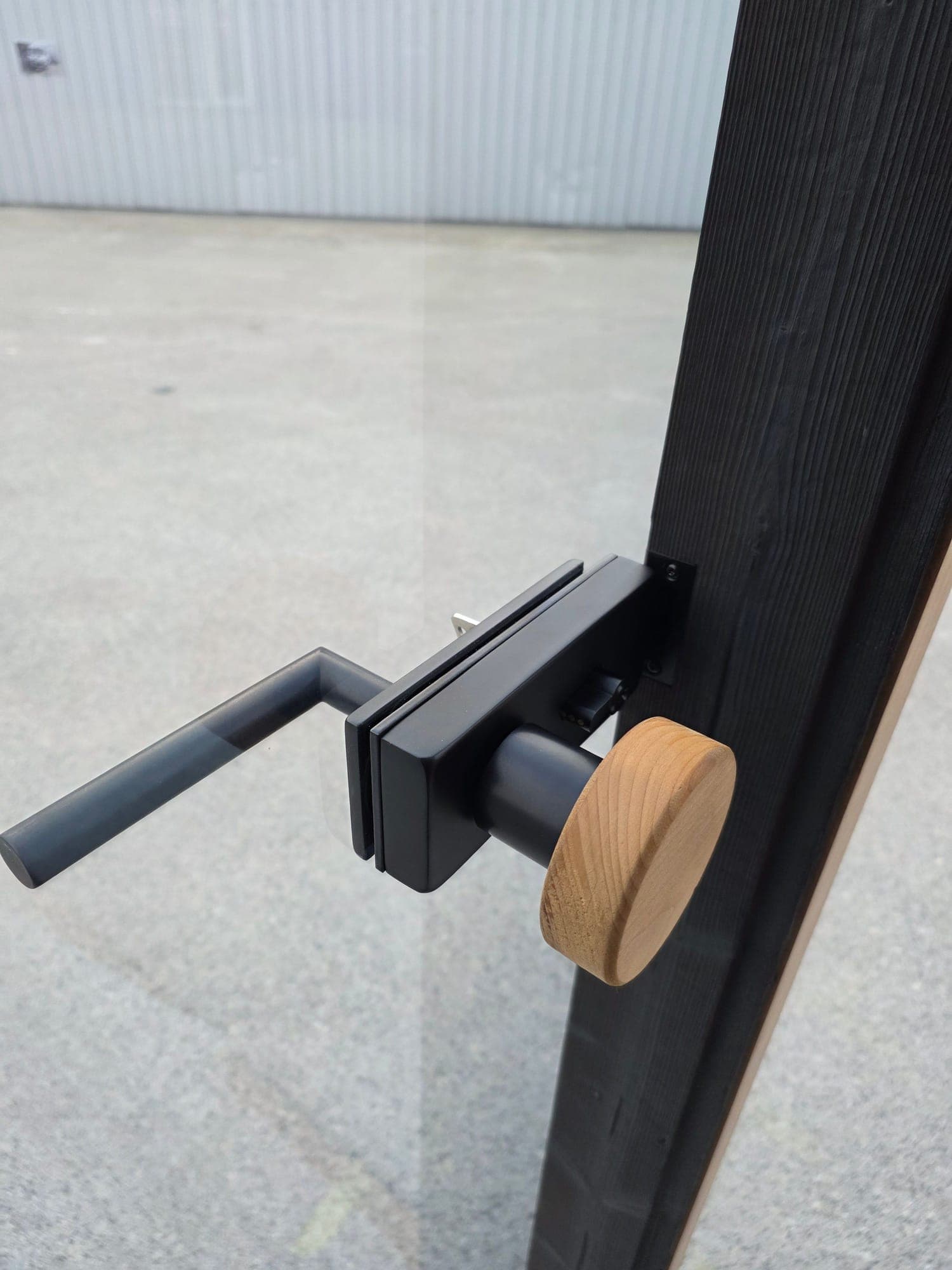 Puxador preto e botão rotativo em madeira na porta em vidro de uma sauna cúbica da Wood Architects